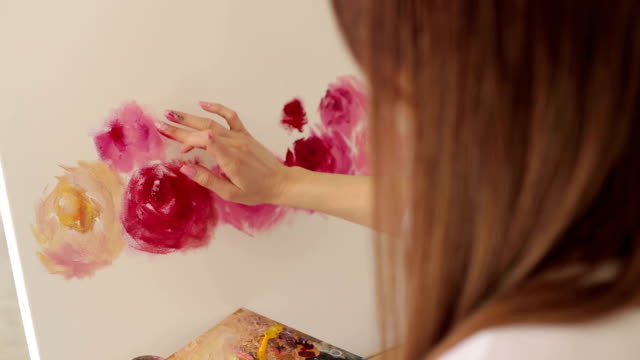 Close-up-of-the-artist's-girl's-hand-on-the-canvas,-she-draws-flowers.
