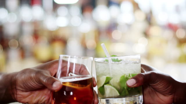 Close-Up-Of-Hands-Holding-Beer-And-Cocktail-Making-A-Toast-In-Bar