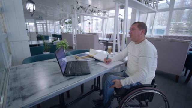 Hombre-dueño-de-éxito-restaurante-inválido-en-silla-de-ruedas-utiliza-tecnología-informática-moderna-para-la-gestión-y-desarrollo-de-ideas-de-negocio