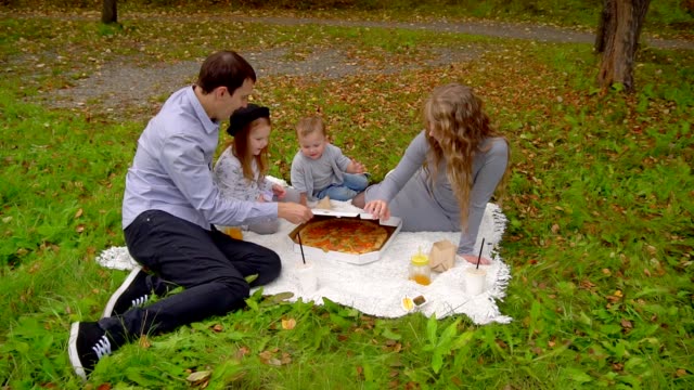 Familie-im-Herbst-Park-Essen-Pizza-auf-dem-Rasen