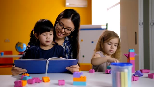 Chica-asiática-preescolar-lectura-con-maestros