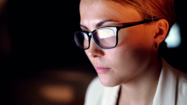 Headshot-of-attractive-young-businesswoman-working-late-at-night-in-office-alone,-a-reflection-of-computer-screen-is-visible-in-her-glasses.-People-and-job-concept.