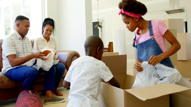 Front-view-of-young-black-family-unpacking-cardboard-boxes-in-a-comfortable-home-4k