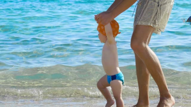 De-vacaciones-una-mamá-da-los-primeros-pasos-a-su-pequeño-bebé-en-la-playa-paso-a-paso-el-recién-nacido-aprende-a-caminar...