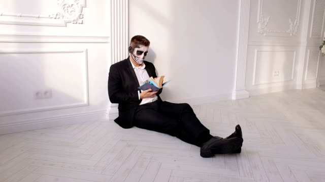 Un-hombre-con-maquillaje-para-Halloween-está-sosteniendo-un-libro-y-hominando-páginas.