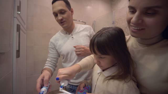 Higiene-matutina,-madre-joven-y-Papi-enseñando-a-la-niña-con-cepillo-dental-dientes-en-frente-del-espejo