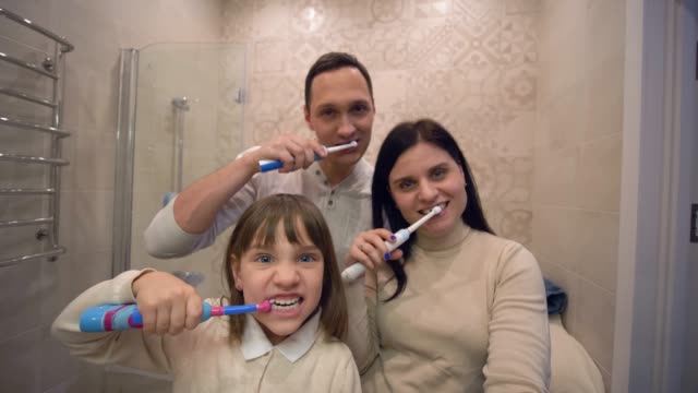 Familiäre-Zähne-putzen,-hübsches-kleines-Mädchen-mit-Eltern-mit-Zahnbürste-putzen-Zähne-vor-dem-Spiegel