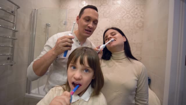 Morgenpflege,-gesundes-kleines-Mädchen-mit-Familie-mit-Zahnbürstenpinsel-Zähne-vor-dem-Spiegel