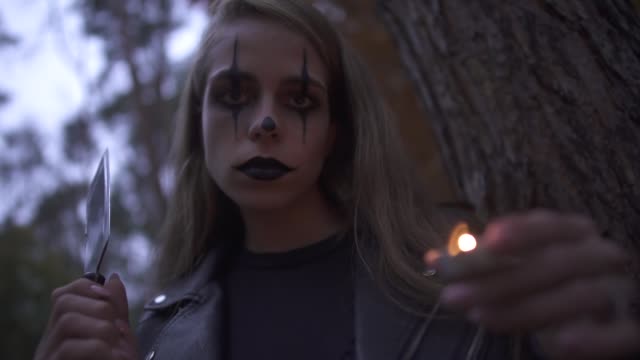Pretty-blonde-psycho-girl-with-horrifying-Halloween-make-up-holding-hatchet-and-small-candle-in-hands