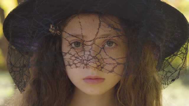 Close-up-of-a-redhead-Caucasian-girl-in-Halloween-witch-hat-standing-in-the-autumn-park.