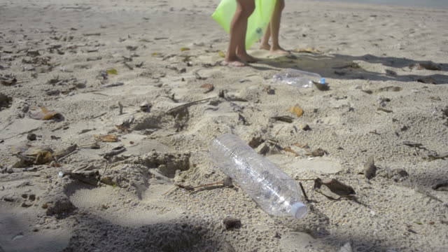 Mamá-y-su-hija-recogiendo-basura-en-la-playa-de-arena-en-una-bolsa-de-plástico-verde,-las-botellas-de-plástico-se-recogen-en-la-playa,-los-voluntarios-limpiando-la-playa.