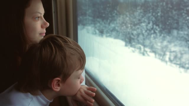 Mom-and-son-are-looking-in-window-in-moving-train-on-winter-landscape.