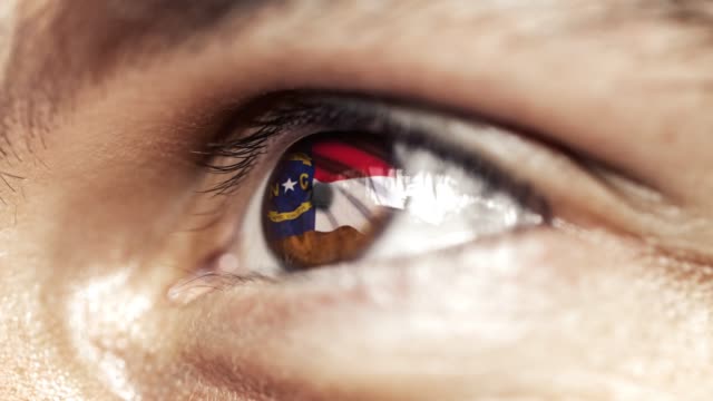 Hombre-con-el-ojo-marrón-de-cerca,-la-bandera-del-estado-de-Carolina-del-Norte-en-iris,-estados-unidos-de-América-con-movimiento-de-viento.-concepto-de-vídeo