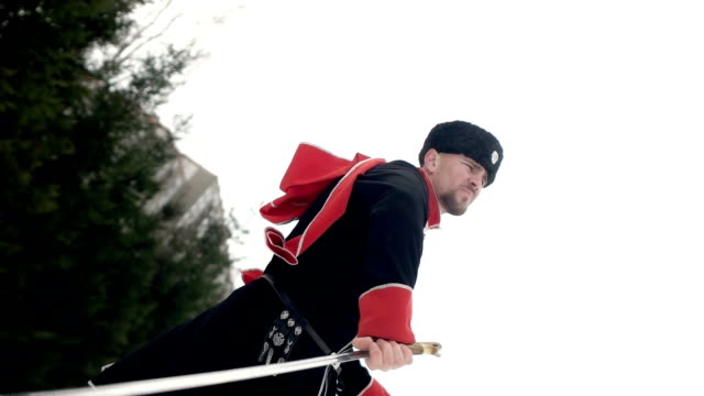 A-young-man-in-Cossack-clothes-swinging-a-sword-in-a-winter-landscape-in-the-snow.