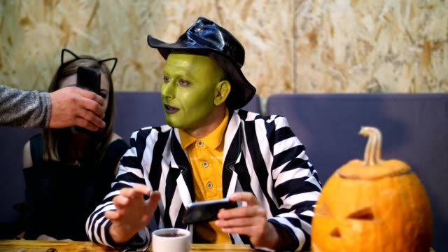 Halloween-Party,-ein-Mann-mit-einem-grünen-Gesicht,-tragen-einen-Hut-und-ein-Mädchen,-gekleidet-in-Katze-Kostüm-suchen-in-das-Telefon,-etw,-lesen,-sprechen