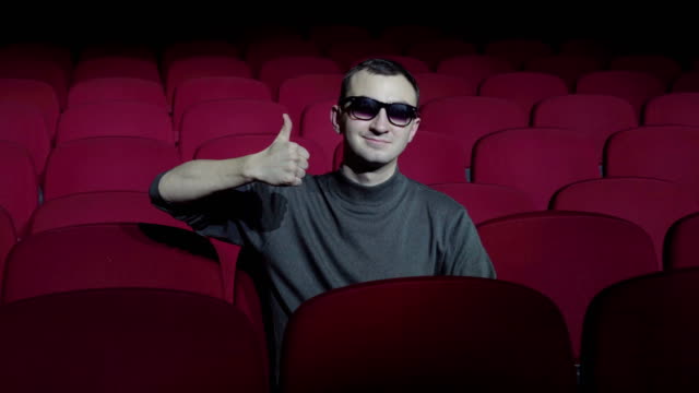 Single-man-sitting-in-comfortable-red-chairs-in-dark-cinema-theater-and-showing-thumbs-up.