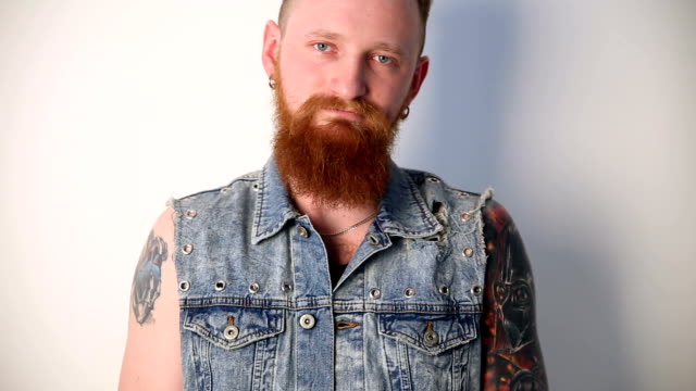 modern-youth.-calm-portrait-of-a-good-biker-with-tattoos-and-a-stylish-beard-and-mustache-in-a-denim-waistcoat.