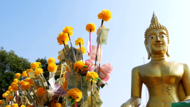 Thai-paper-money-on-a-branch-of-the-Marigold-on-the-background-of-big-golden-Buddha,-Pattaya.-Thailand