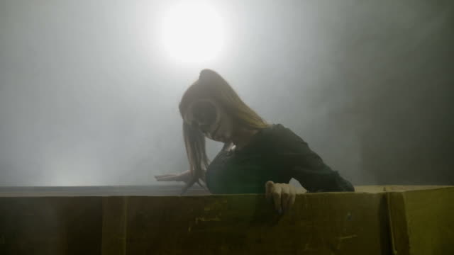 Young-teenager-female-zombie-waking-up-from-the-dead-getting-out-from-her-coffin-on-a-gray-smoke-background-with-fog-on-halloween-night