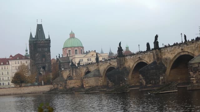 The-Charles-Bridge-on-the-background-of-the-old-tower-and-the-green-dome-of-the-cathedral-in-Prague,-side-view,-tourists-stroll-along-the-Charles-Bridge,-Prague,-October-19,-2017