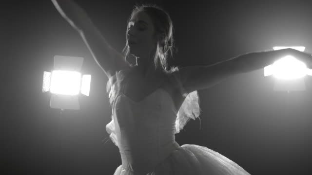 Professional-ballerina-dancing-ballet-in-spotlights-on-big-stage.-Beautiful-caucasian-young-girl-wearing-white-tutu-dress.-Black-and-white-vintage-retro-effect-tonned.-4k