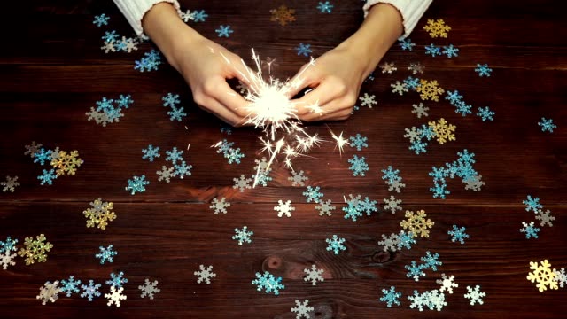 Female-hands-holding-a-burning-sparkler-over-wooden-table-with-decorations