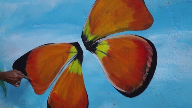 Pintor-mural-dibuja-mariposas-en-color-en-la-pared-de-la-escuela