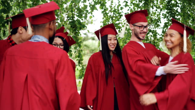 Amigos-alegres-graduar-estudiantes-en-trajes-y-birretes-son-felicitando-mutuamente-después-de-la-ceremonia-de-graduación,-son-abrazos-y-risas.