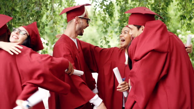 Slow-Motion-der-glücklichen-Absolventen-tragen-Kleider-und-Mörtel-Boards,-umarmen,-lachen-und-gratulieren-einander-am-Abschlusstag.-Glück-und-Jugend-Konzept.