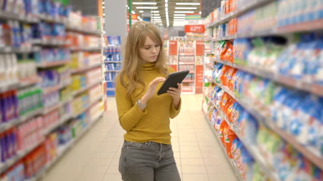 Joven-mujer-de-compras-en-el-hipermercado-y-buscando-información-sobre-los-productos-en-su-tablet