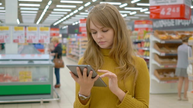 Women-shopping-at-the-supermarket-and-using-mobile-apps-on-her-tablet