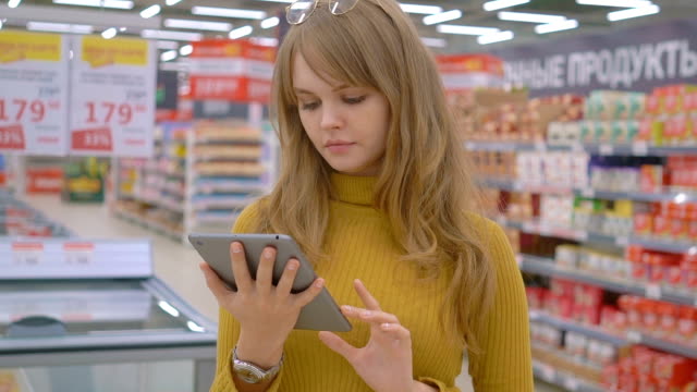 Women-shopping-at-the-supermarket-and-using-mobile-apps-on-her-tablet