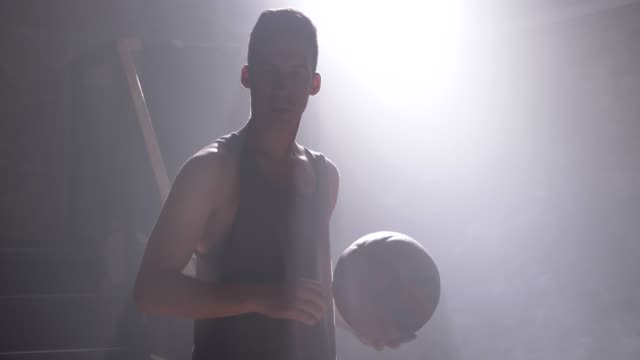 Hombre-alto-realizando-baloncesto-slam-dunk-en-gimnasio-oscuro-con-humo