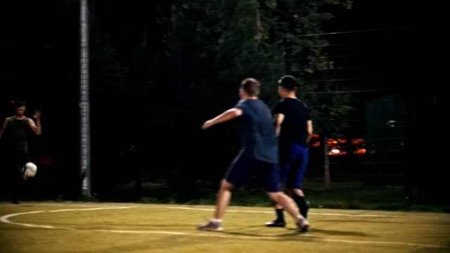 Junger-Mann-tritt-einen-Ball,-der-fliegt-vorbei-an-andere-Fußballer-und-hinter-dem-Tor,-Nacht-schießen-Fußballspiel