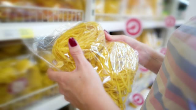 Closeup-caucasian-woman-near-shop-shelves-and-choosing-pasta-in-grocery-market