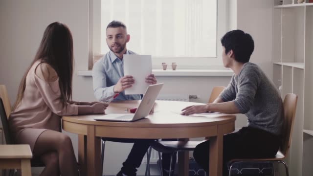 Beautiful-woman-boss-listening-to-young-Japanese-man-at-job-interview-in-modern-office,-Caucasian-employee-joins-in