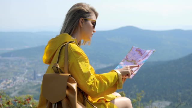 Wanderer-in-einem-gelben-Regenmantel,-Blick-auf-Karte-von-Berg.-Frau-mit-Karte-in-Bergen-FullHD