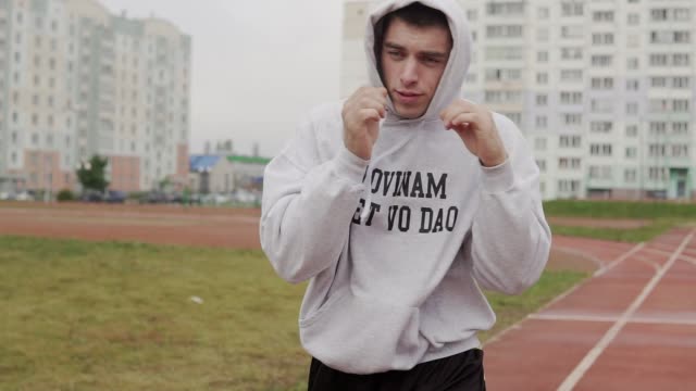 Young-man-training-in-hoodie-boxing-with-invisible-opponent-at-stadium.