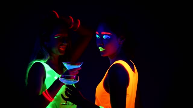 Women-with-UV-face-paint,-laser,-glowing-bracelets,-drinks,-glowing-clothing-dancing-together-in-front-of-camera,-Half-body-shot.-Caucasian-and-asian-woman.-.