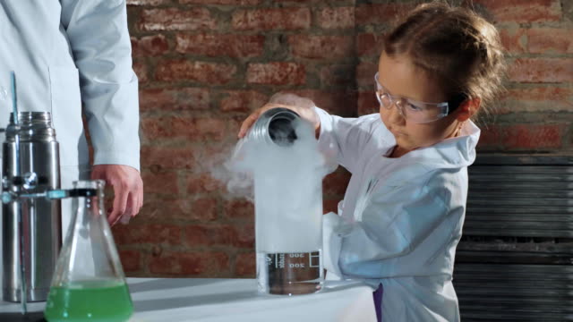 Child-scientist-pouring-liquid-nitrogen-from-steel-thermos-bottle-in-beaker
