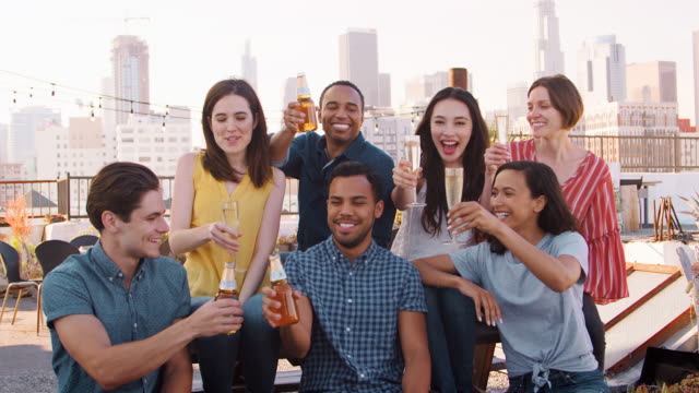 Friends-Gathered-On-Rooftop-Terrace-For-Party-With-City-Skyline-In-Background-Making-Toast-With-Drinks