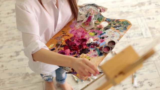 Ein-junges-Mädchen-in-einem-weißen-Hemd-stützt-sich-auf-Leinwand-im-Atelier.-Kunst.
