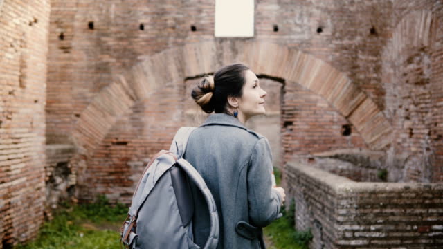 Back-view-of-excited-young-female-student-researcher-with-backpack-and-map-exploring-ancient-ruins-in-Ostia,-Italy.