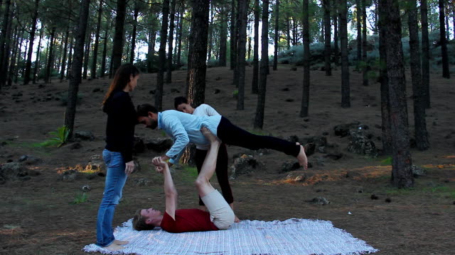 Paar-von-männlichen-Yogis-praktizieren-Acro-Yoga-mit-Aufsicht-von-LehrerInnen-im-Waldpark