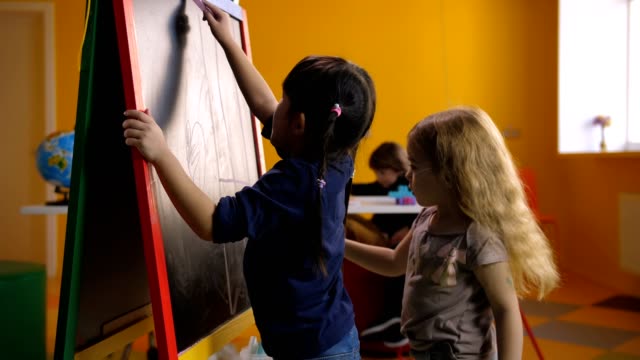 Cheerful-multi-ethnic-girls-drawing-on-chalkboard