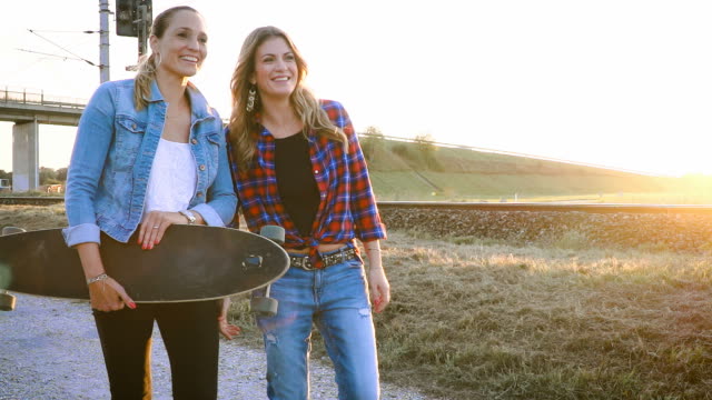 two-beautiful-and-young-women-walking-and-talking-with-skateboard