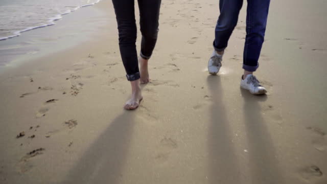 Two-people-strolling-on-seashore-and-holding-hands-together.