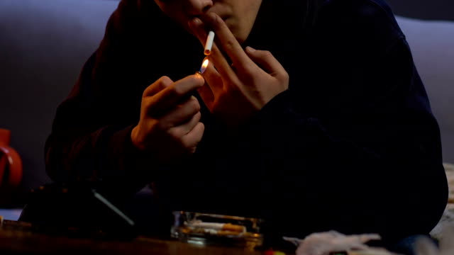 Man-lighting-cigarette-and-smoking-it,-table-with-ashtray-cup-and-joystick