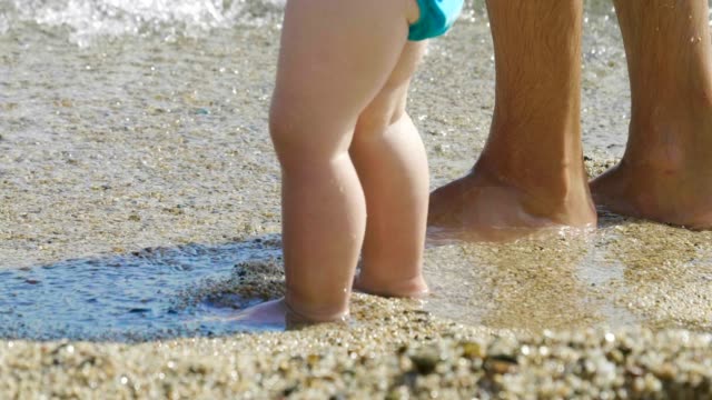 Im-Urlaub-Eine-Mama-macht-die-ersten-Schritte-zu-seinem-kleinen-Baby-am-Strand-Schritt-für-Schritt-lernt-das-Neugeborene-zu-gehen-...