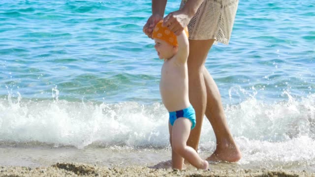 Im-Urlaub-Eine-Mama-macht-die-ersten-Schritte-zu-seinem-kleinen-Baby-am-Strand-Schritt-für-Schritt-lernt-das-Neugeborene-zu-gehen-...
